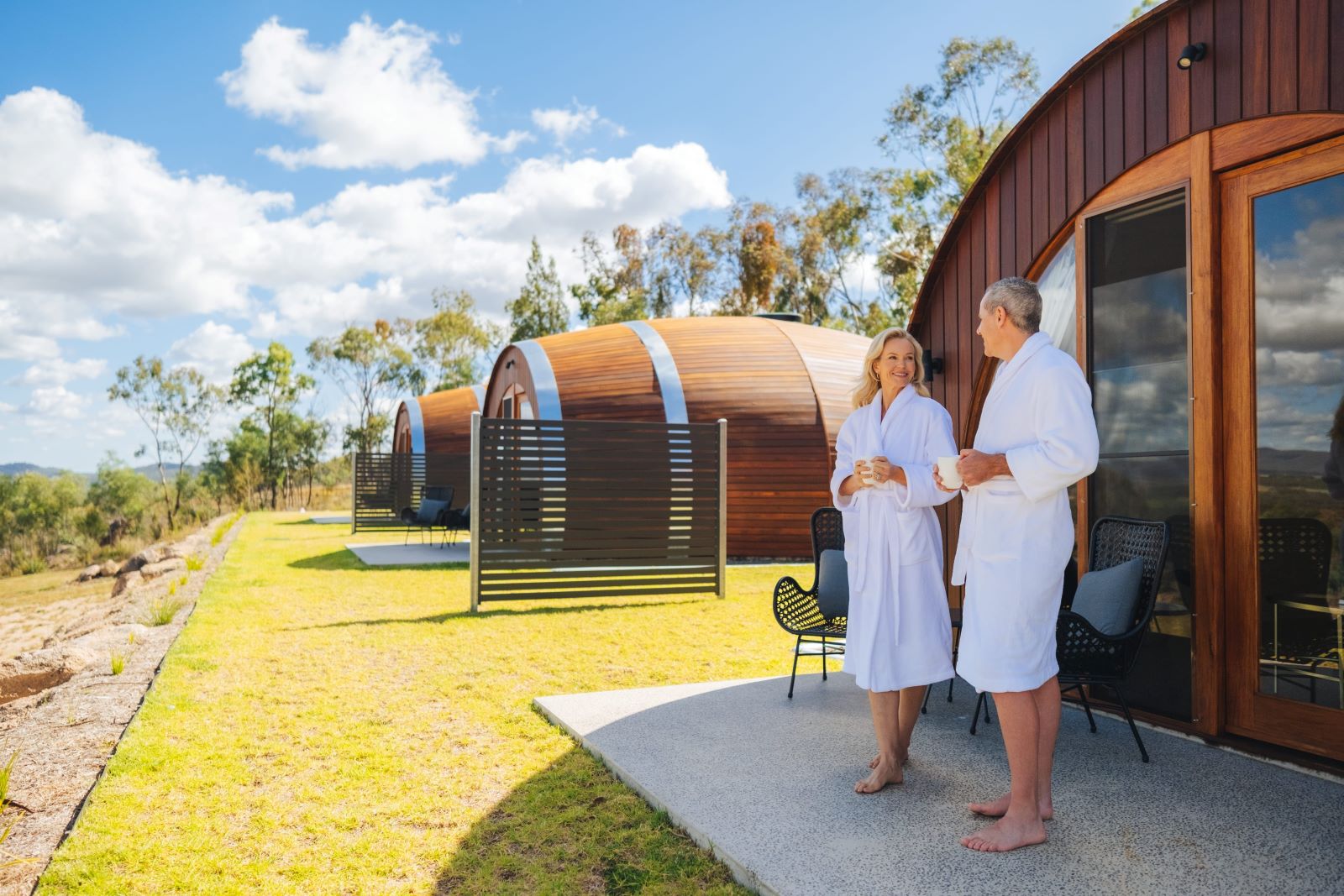 Couple in bathrobes standing outside of giant wine barrel accommodation.